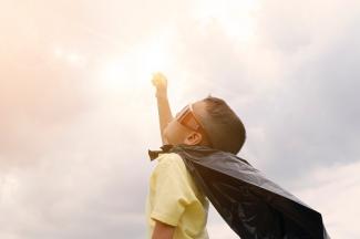 child dressed in a cape looking up towards sky