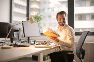 Man at computer desk holding open notebook