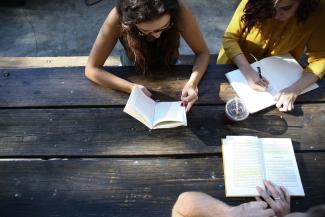 3 older students at picnic table with open books