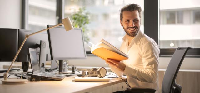 Man at computer desk holding open notebook