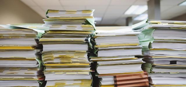 stack of books and files on table by Wesley Tingey courtesy of Unsplash.
